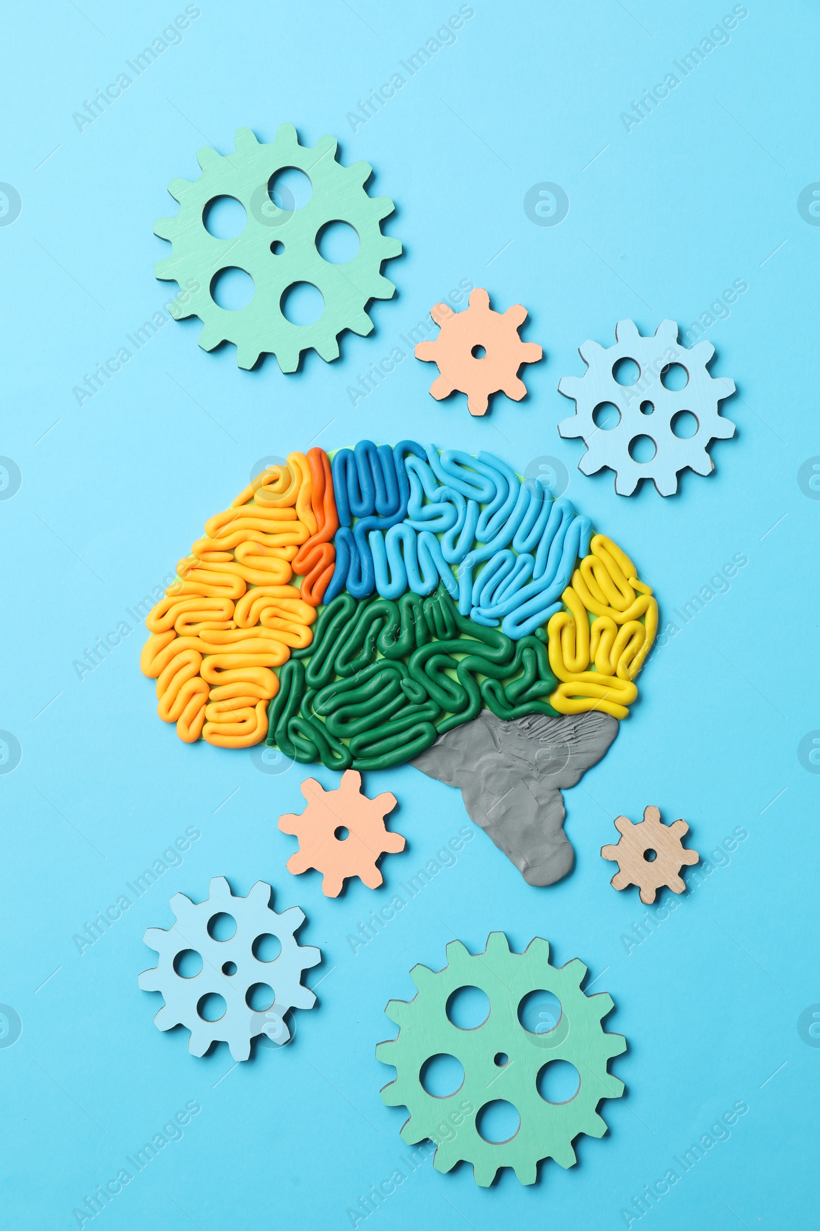 Photo of Amnesia problem. Brain with sections made of plasticine and gears on light blue background, flat lay