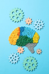 Photo of Amnesia problem. Brain with sections made of plasticine and gears on light blue background, flat lay