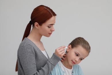 Mother dripping medication into daughter's ear on light grey background