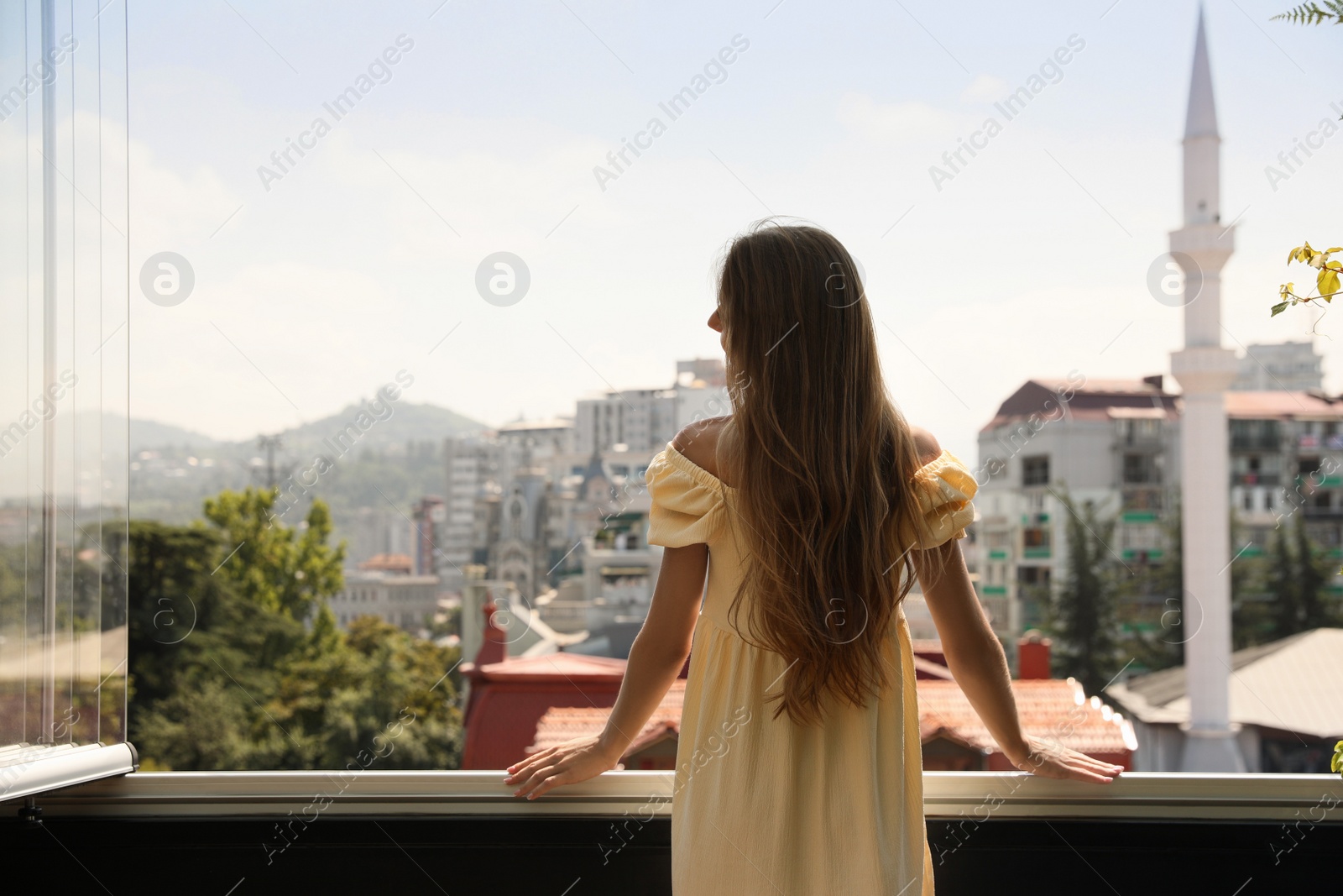 Photo of Young woman standing on balcony, back view. Space for text