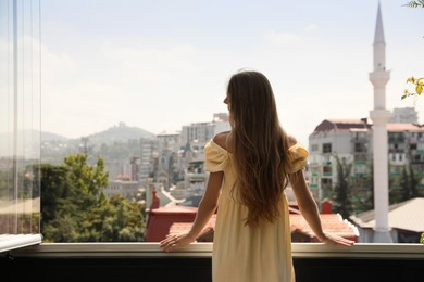 Young woman standing on balcony, back view. Space for text