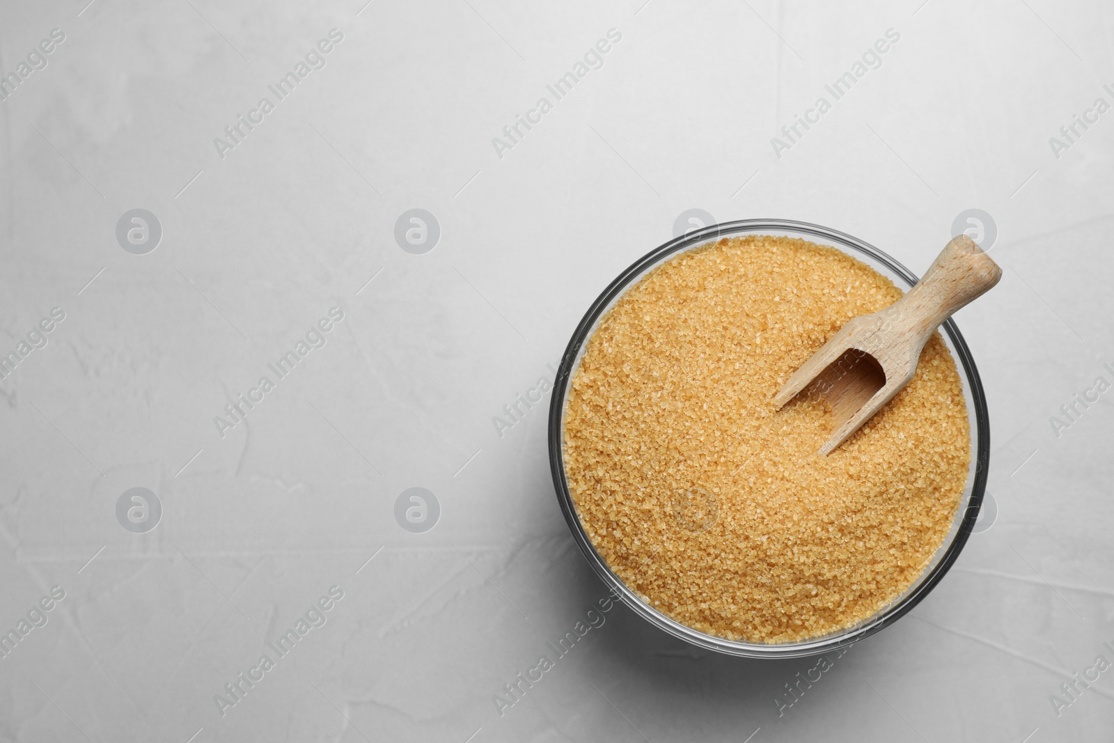 Photo of Brown sugar and scoop in glass bowl on light grey table, top view. Space for text