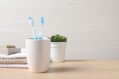 Photo of Plastic toothbrushes in holder, soap, towels and green houseplant on wooden table, space for text