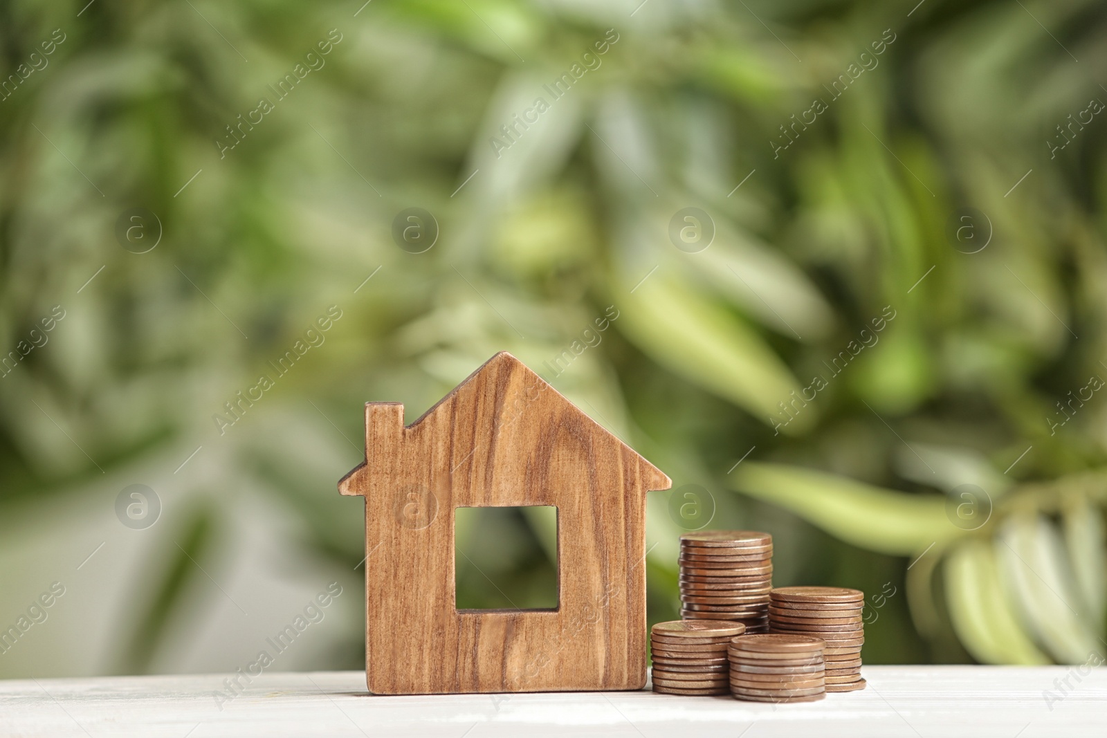 Photo of House model and coins on white table against blurred green background