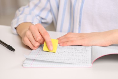 Girl erasing mistake in her notebook at white desk indoors, closeup