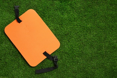 Photo of Orange foam tourist seat mat on green grass, top view. Space for text