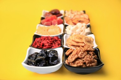 Photo of Bowls with dried fruits and nuts on yellow background, closeup