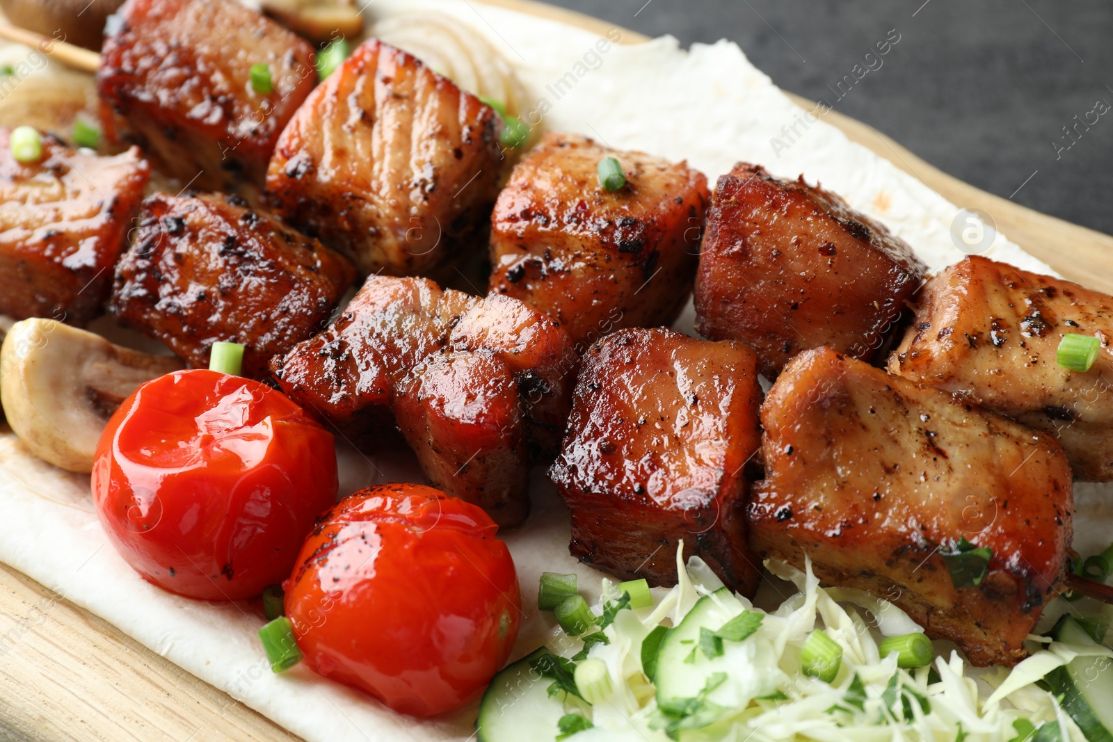 Photo of Delicious shish kebabs with vegetables and lavash on wooden board, closeup