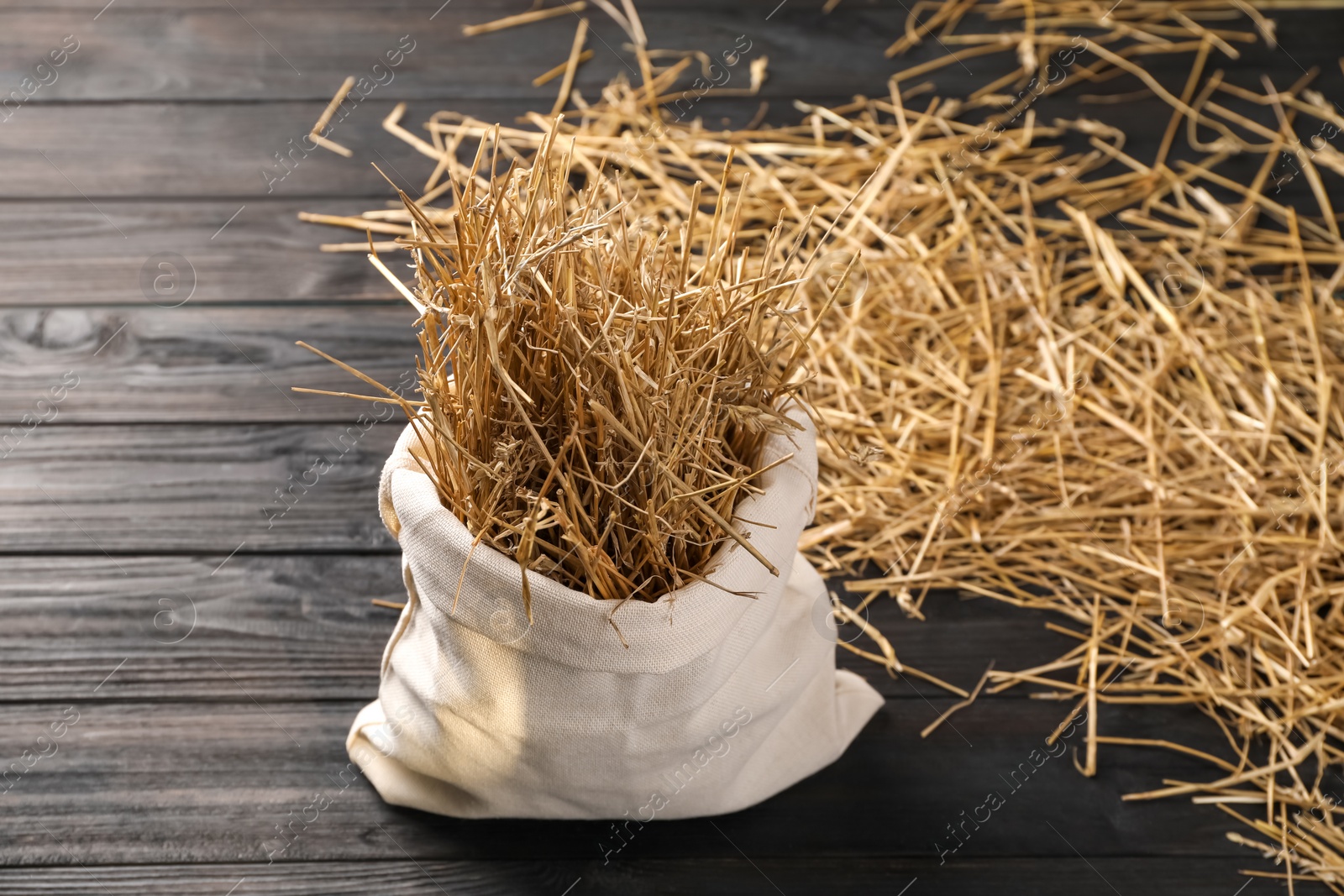 Photo of Dried straw in burlap sack on dark wooden table, space for text