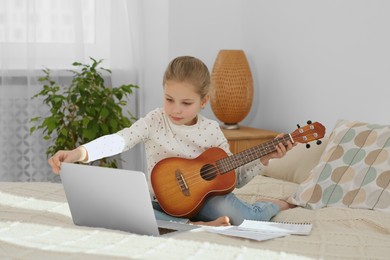 Little girl learning to play ukulele with online music course at home. Time for hobby