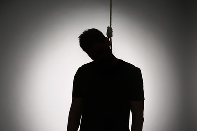 Silhouette of man with rope noose on neck against light background