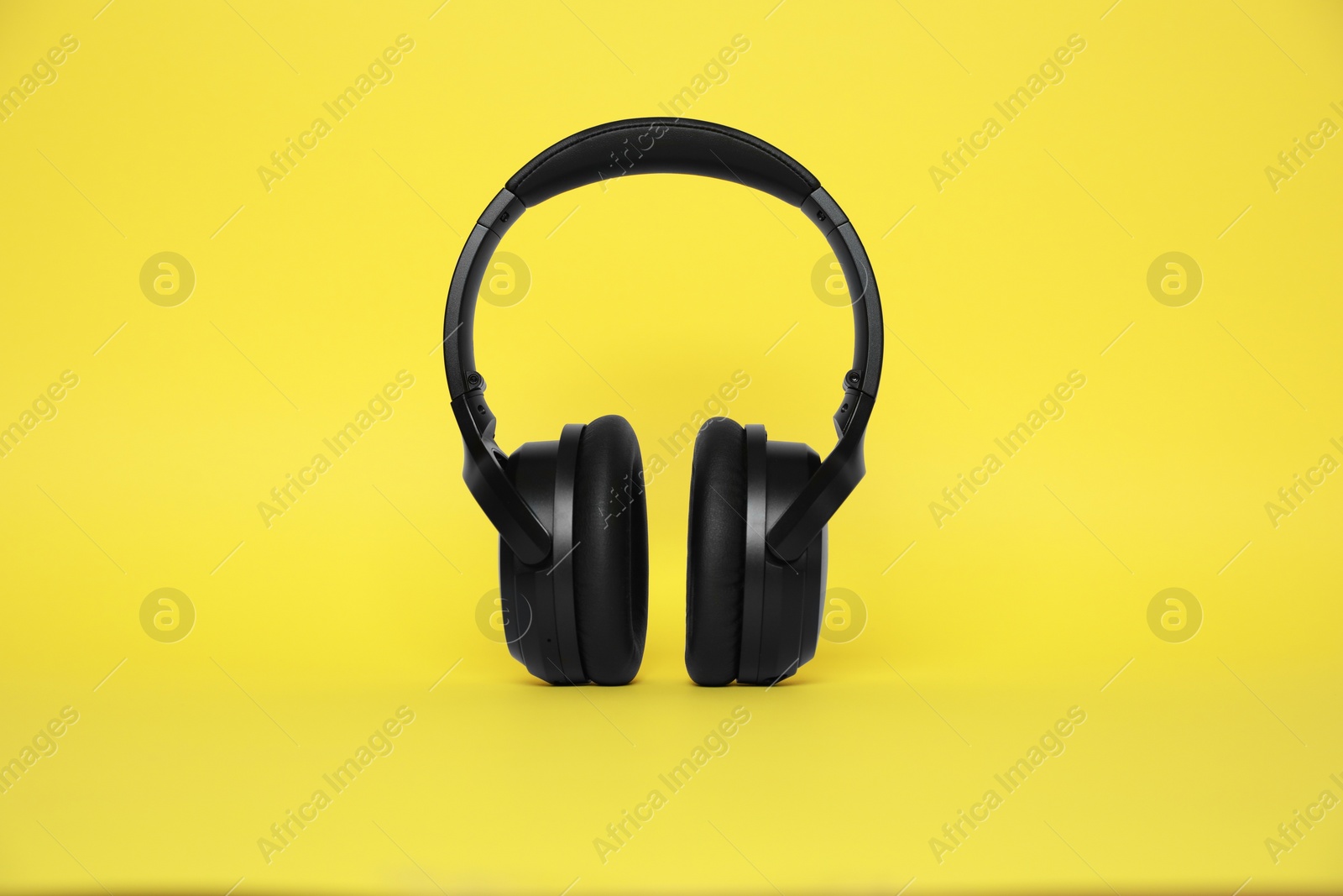Photo of Modern black wireless headphones on yellow background