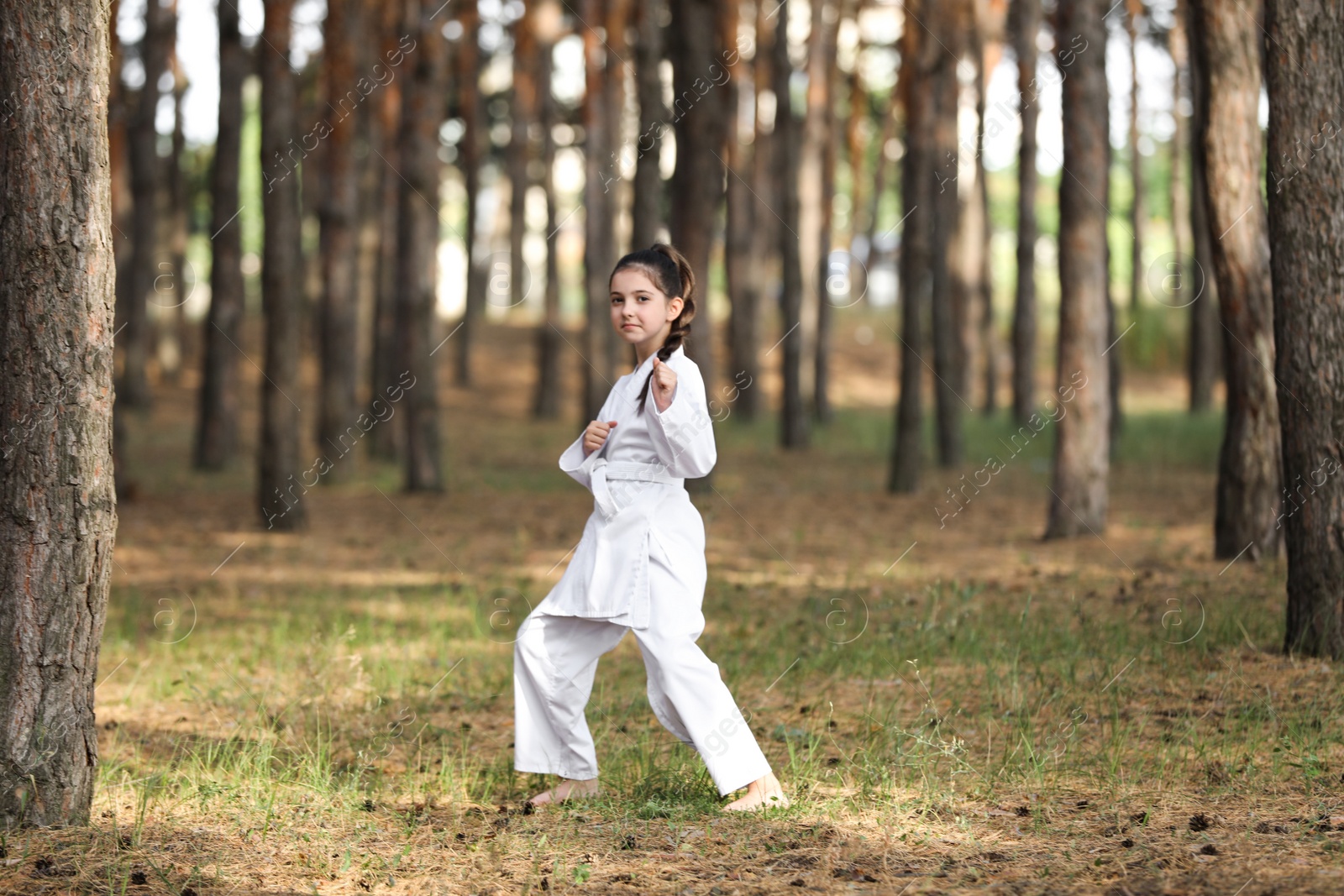 Photo of Cute little girl in kimono practicing karate in forest