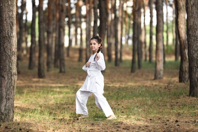 Cute little girl in kimono practicing karate in forest