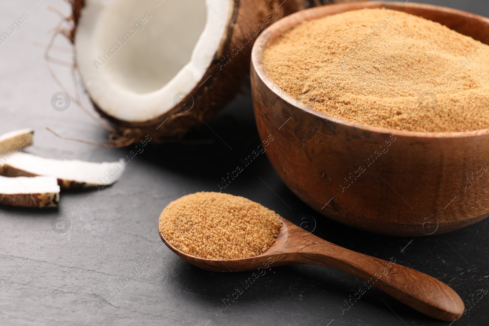 Photo of Spoon with coconut sugar, bowl and fruit on dark textured table, closeup