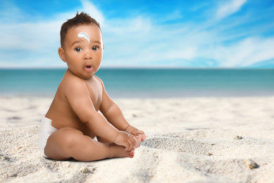 Adorable African American baby with sun protection cream on face at sandy beach, space for text 