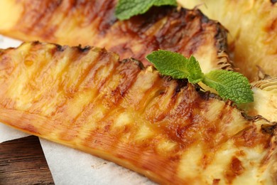 Photo of Tasty grilled pineapple pieces and mint leaves on wooden table, closeup