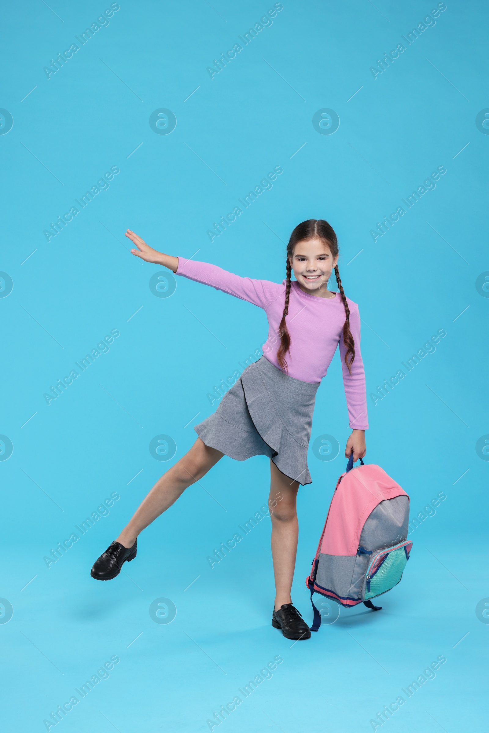 Photo of Cute girl with backpack on light blue background, space for text