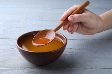 Woman with melted ghee butter at light grey wooden table, closeup