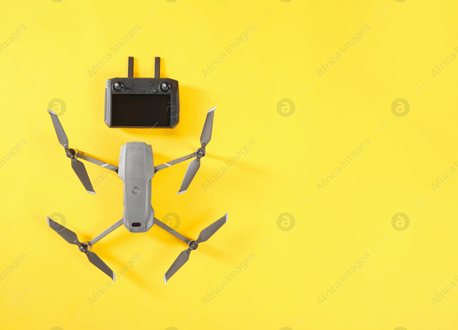 Photo of Modern drone with controller on yellow background, flat lay. Space for text