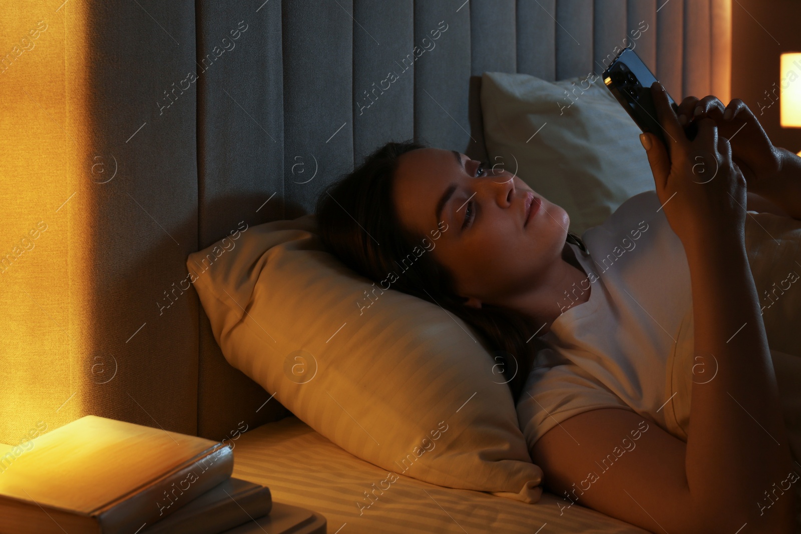 Photo of Woman using smartphone in bed at night. Internet addiction