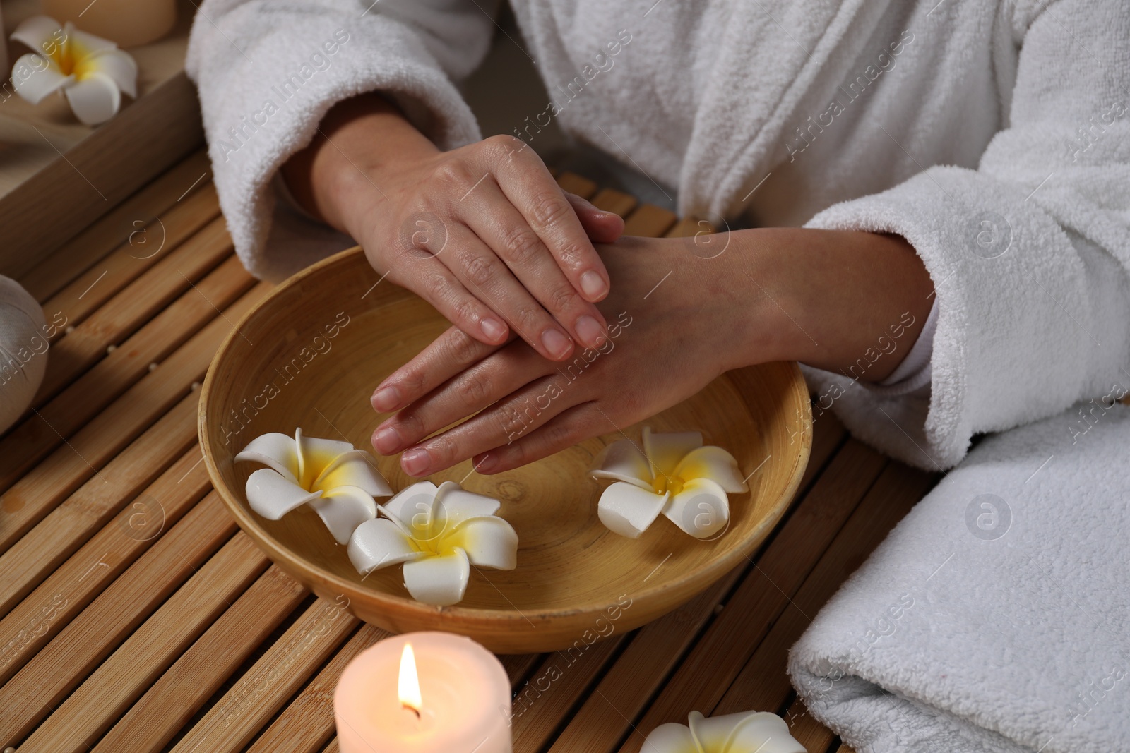 Photo of Woman soaking her hands in bowl of water and flowers at wooden table, closeup. Spa treatment