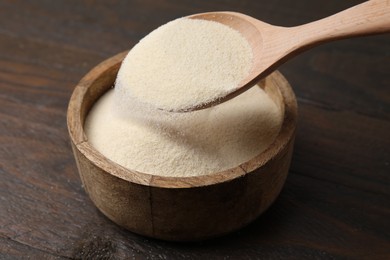 Photo of Pouring uncooked organic semolina into bowl on wooden table, closeup