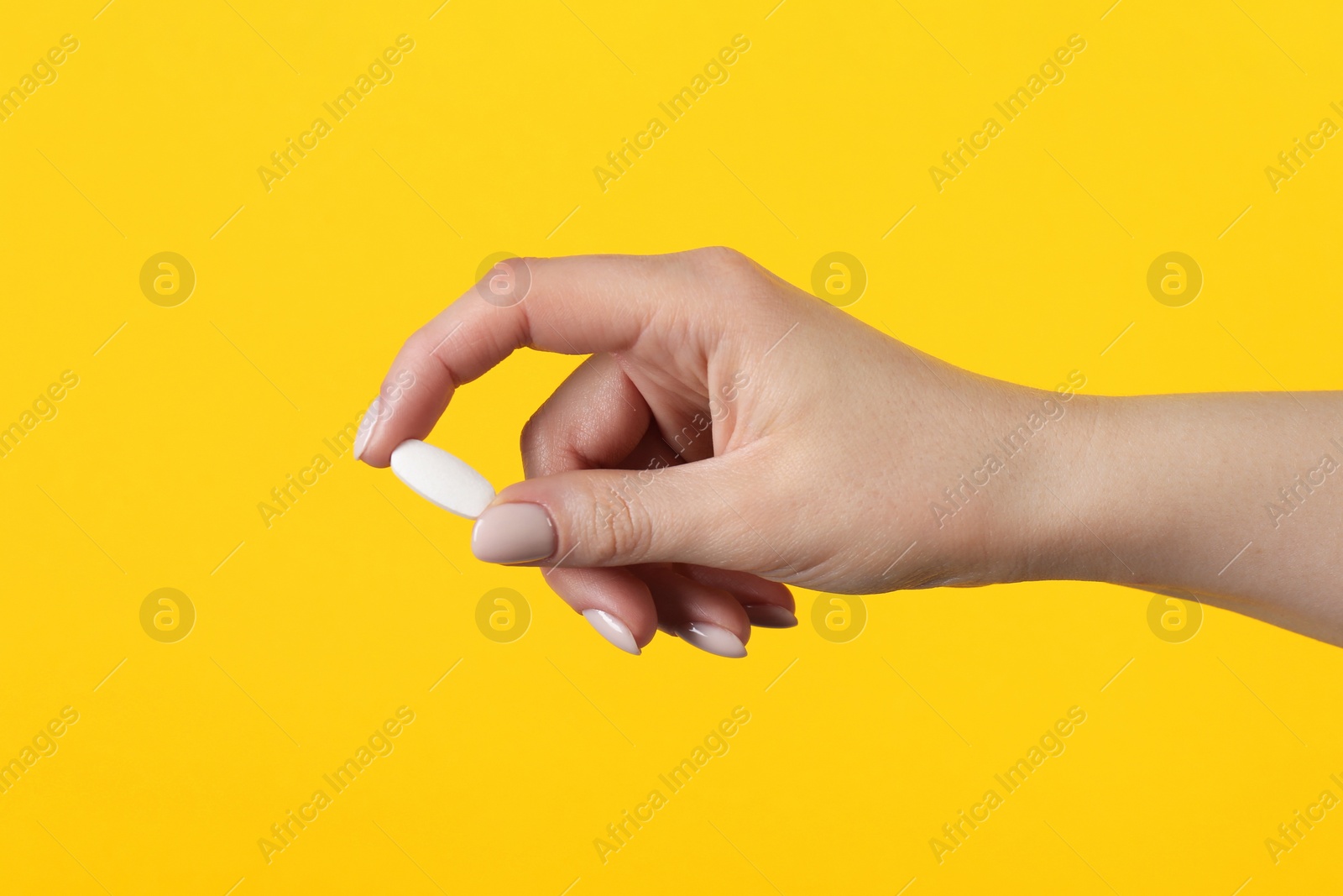 Photo of Woman holding vitamin pill on yellow background, closeup. Health supplement