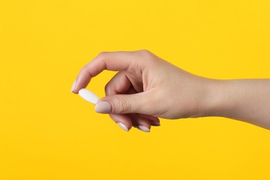 Photo of Woman holding vitamin pill on yellow background, closeup. Health supplement