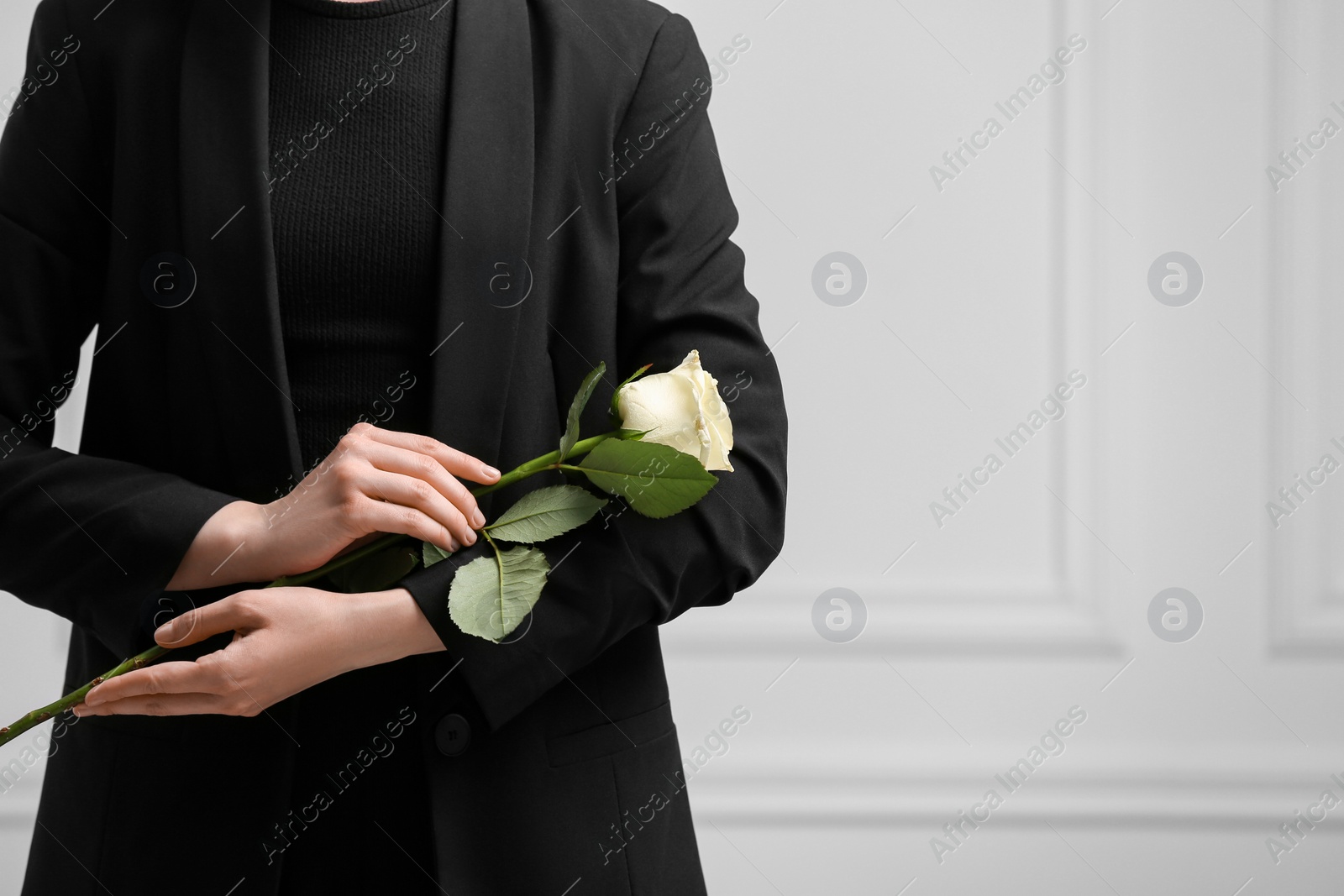 Photo of Woman with rose flower near white wall, closeup and space for text. Funeral ceremony