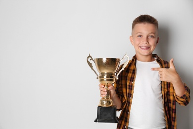 Happy boy with golden winning cup on light background. Space for text