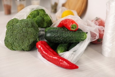 Plastic bags and fresh vegetables on white table