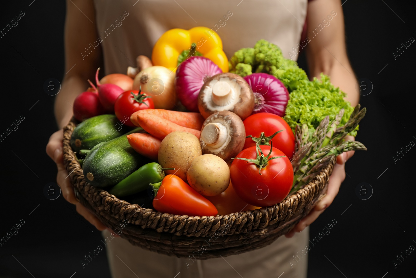 Photo of Woman holding wicker basket full of fresh vegetables on black background, closeup