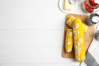 Fresh corn cobs with butter on white wooden table, flat lay. Space for text