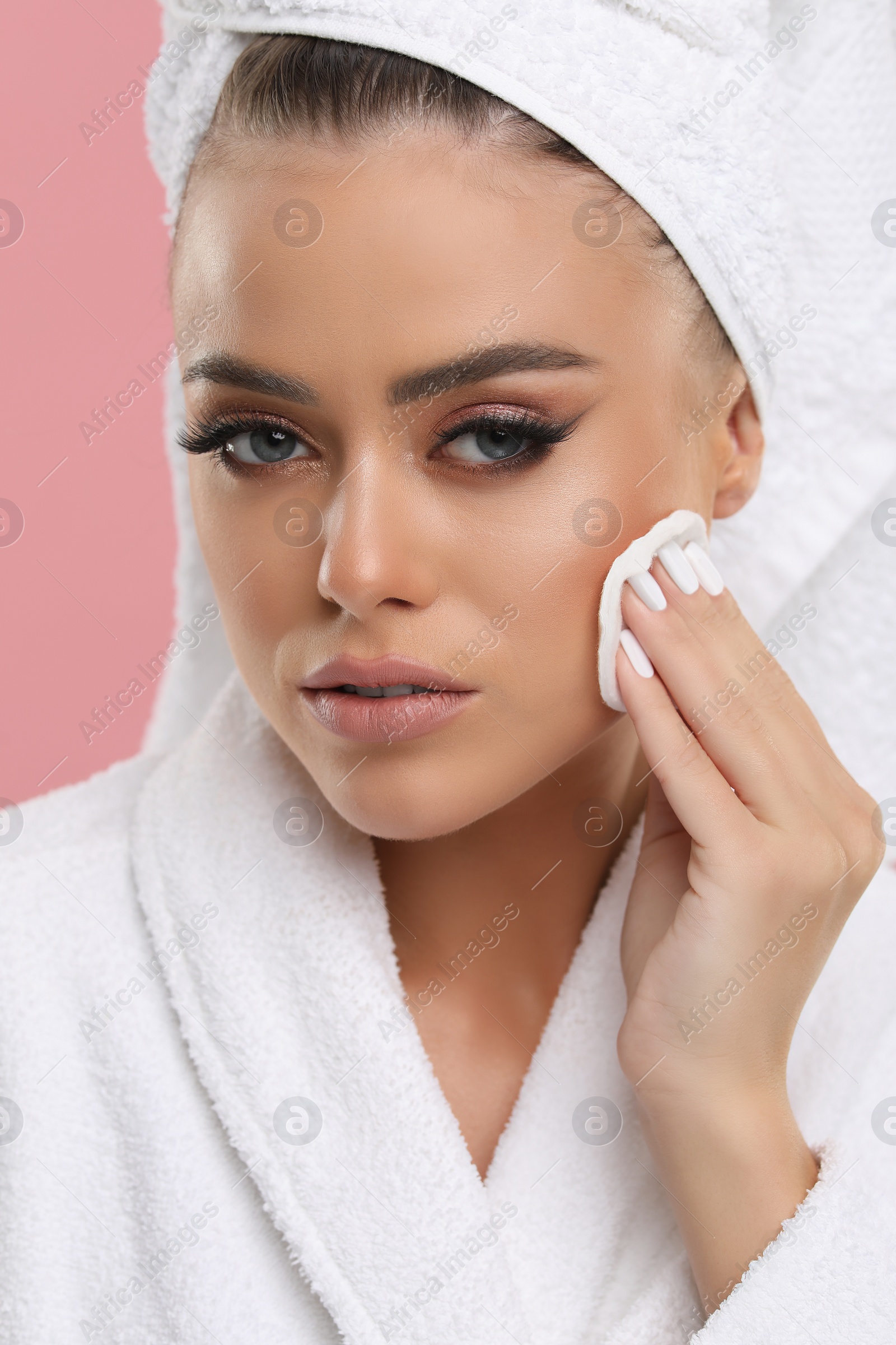 Photo of Beautiful woman removing makeup with cotton pad on pink background