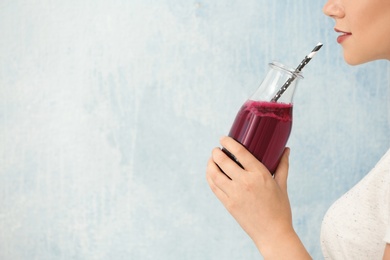 Woman holding bottle of beet smoothie on light background with space for text, closeup