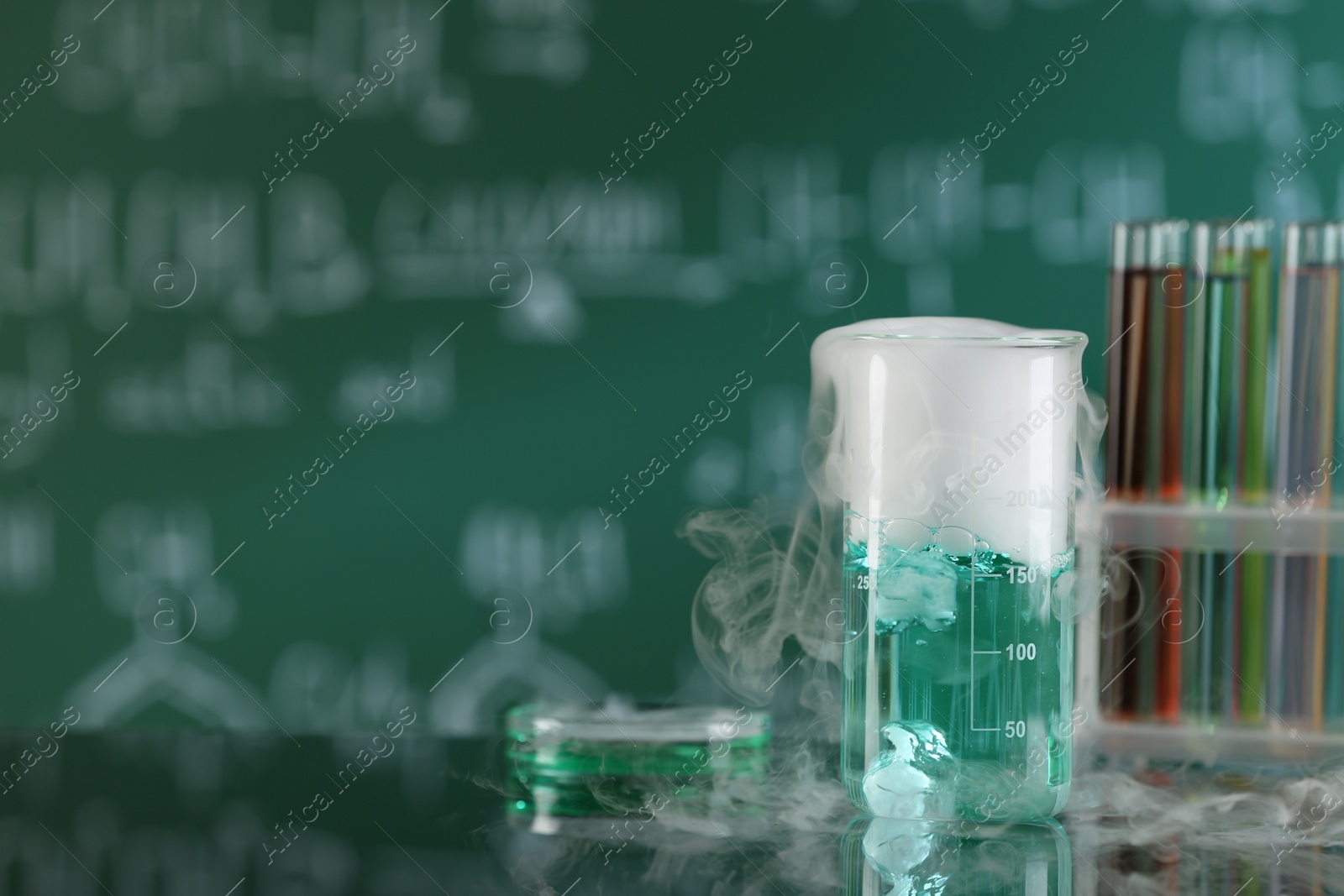 Photo of Laboratory glassware and test tubes with colorful liquids on glass table, space for text. Chemical reaction