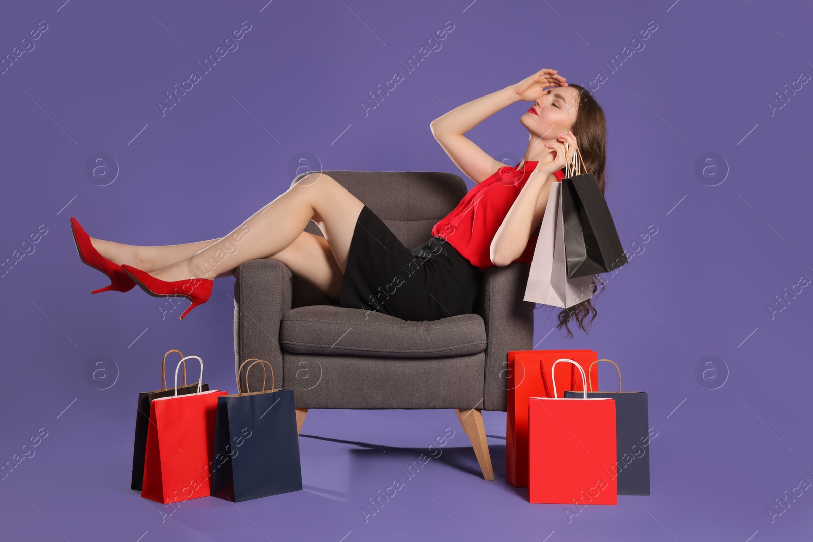 Photo of Beautiful woman relaxing on armchair and holding shopping bags against purple background