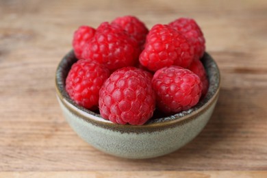 Photo of Tasty ripe raspberries in bowl on wooden table, closeup