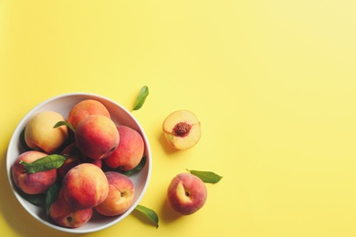 Photo of Fresh ripe peaches and green leaves on yellow background, flat lay. Space for text