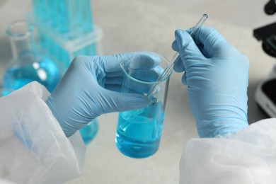 Scientist taking sample of light blue liquid in laboratory, closeup