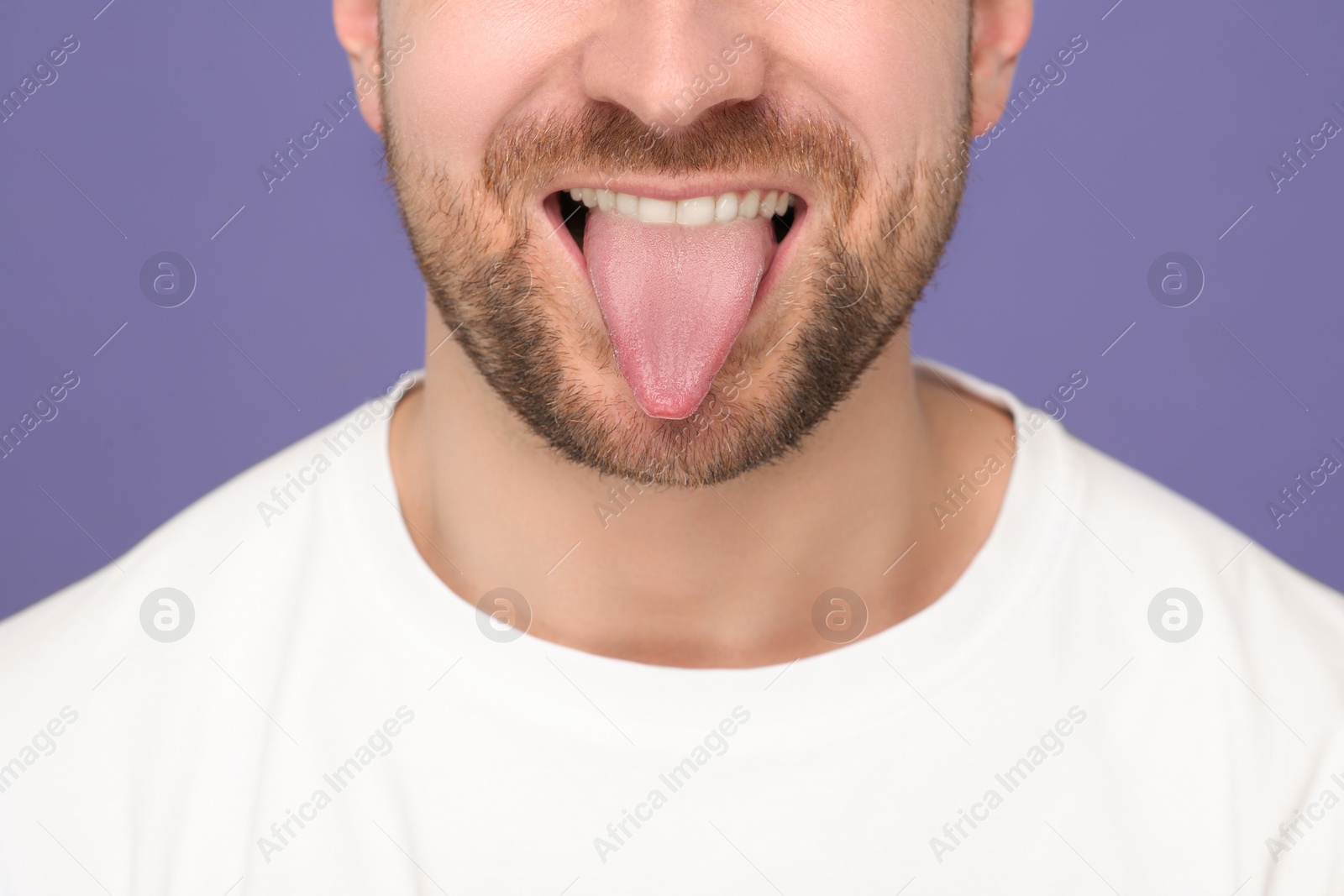 Photo of Man showing his tongue on purple background, closeup