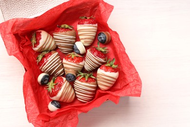 Photo of Box with delicious chocolate covered strawberries and blueberries on white table, top view. Space for text