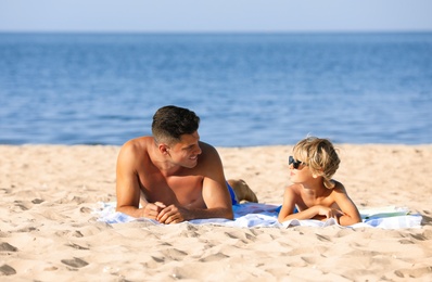 Photo of Father and son lying on sandy beach near sea. Summer holidays with family