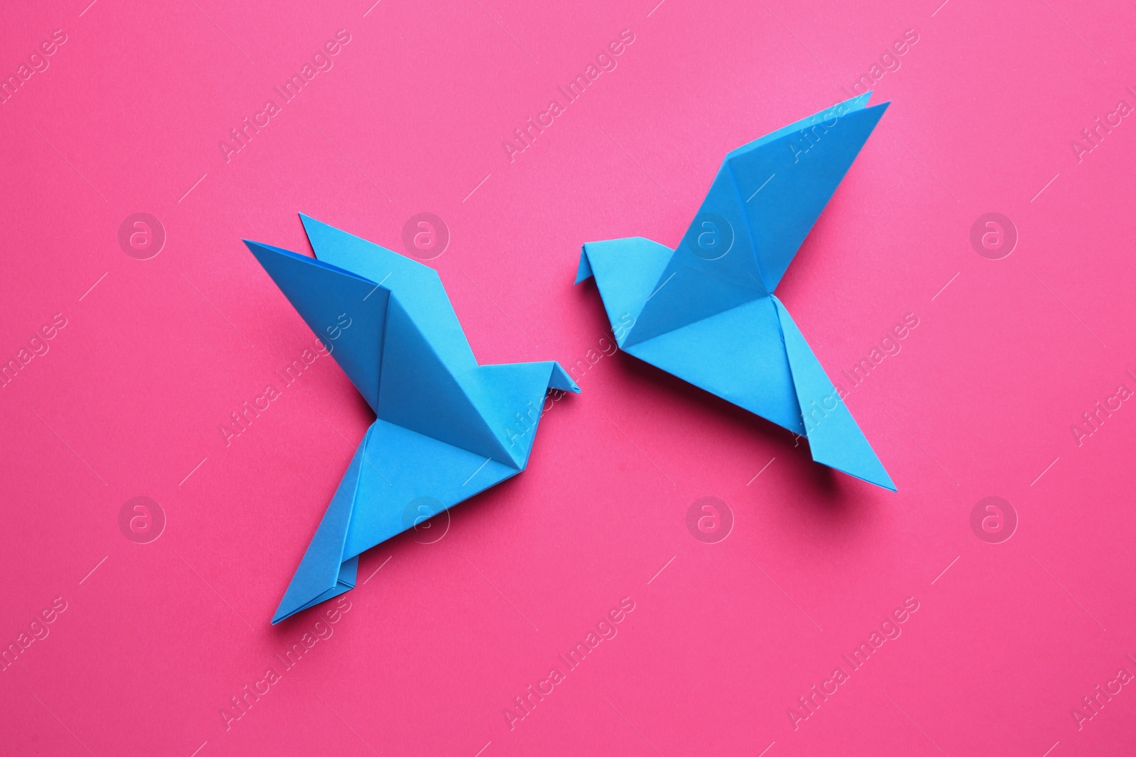 Photo of Beautiful light blue origami birds on pink background, flat lay