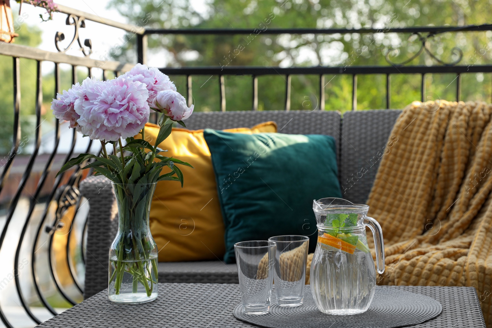 Photo of Rattan table with jug of water, glasses and beautiful flowers on terrace