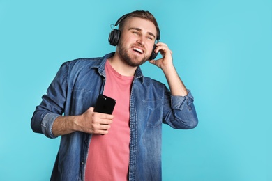 Handsome man with mobile phone enjoying music in headphones on color background. Space for text