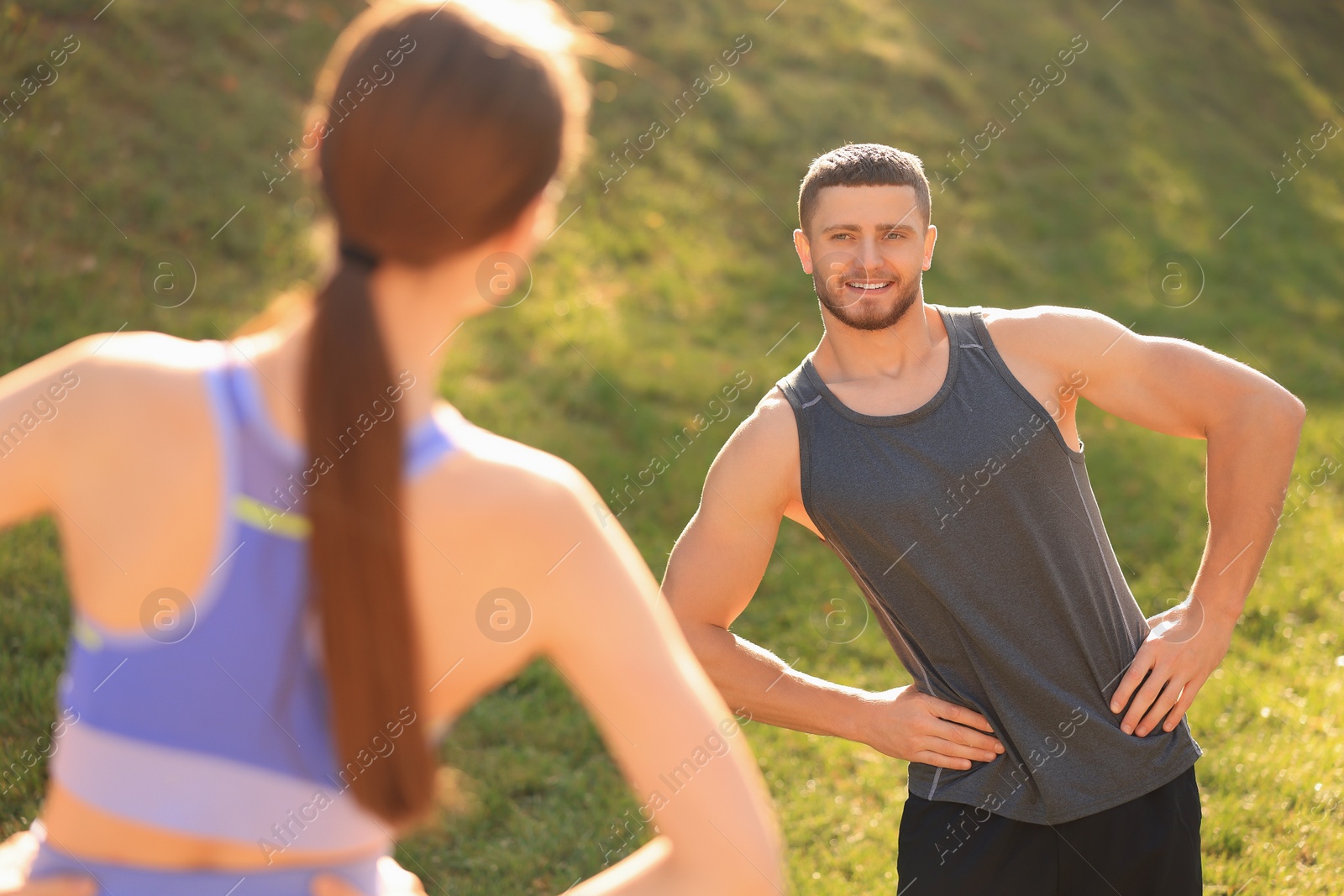 Photo of Attractive couple doing sports exercises in park on sunny day. Stretching outdoors