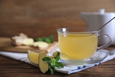 Photo of Glass of aromatic ginger tea and ingredients on wooden table, closeup. Space for text