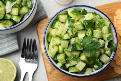 Photo of Bowl of delicious cucumber salad served on light table, flat lay